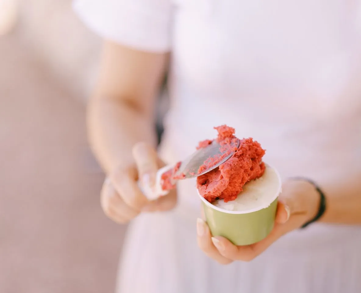 Personne tenant un gobelet vert avec de la glace pilée rouge et une cuillère, vue rapprochée.