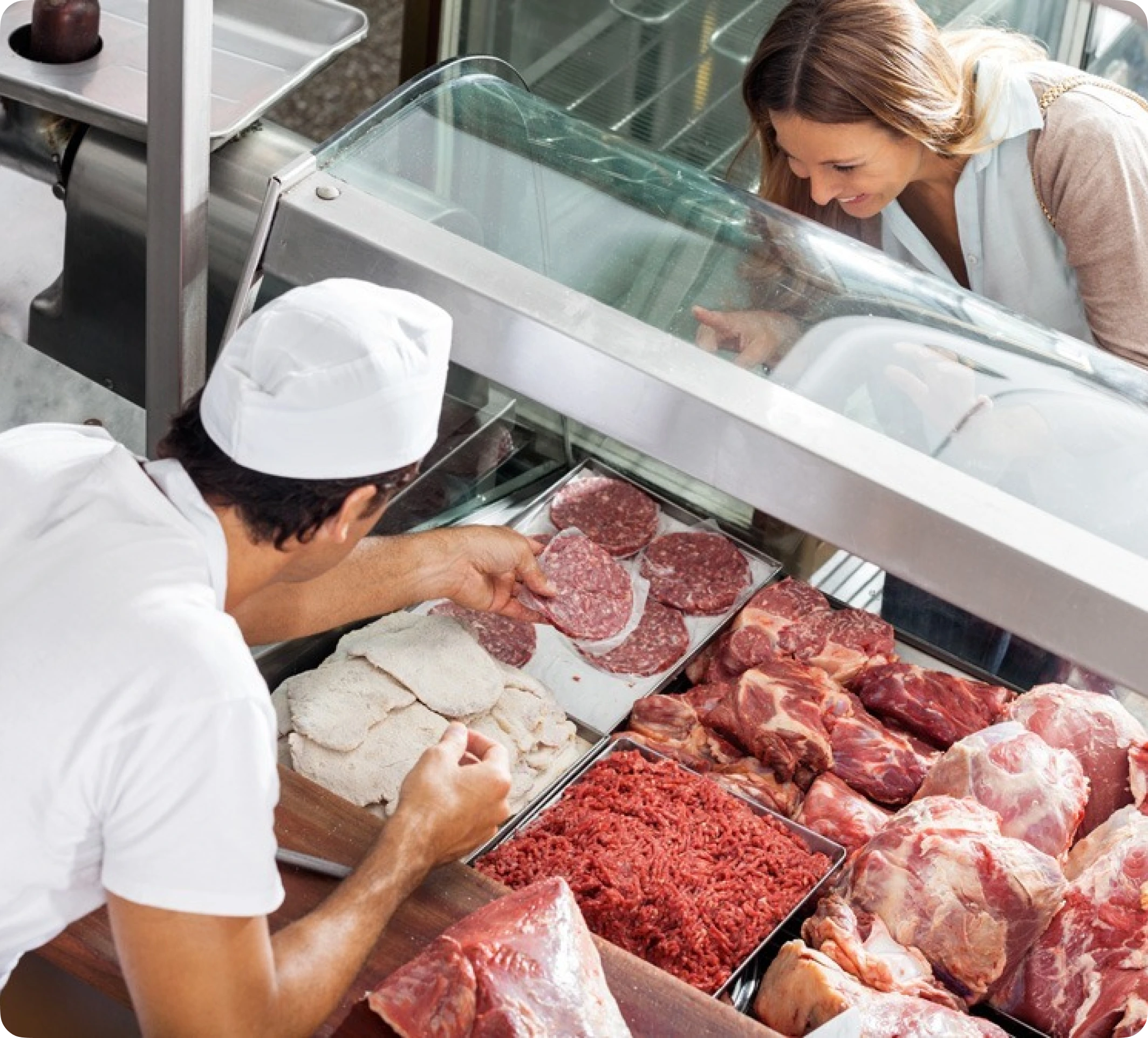 Intérieur de boucherie : boucher derrière un comptoir réfrigéré présentant viandes et charcuteries, caisse tactile.