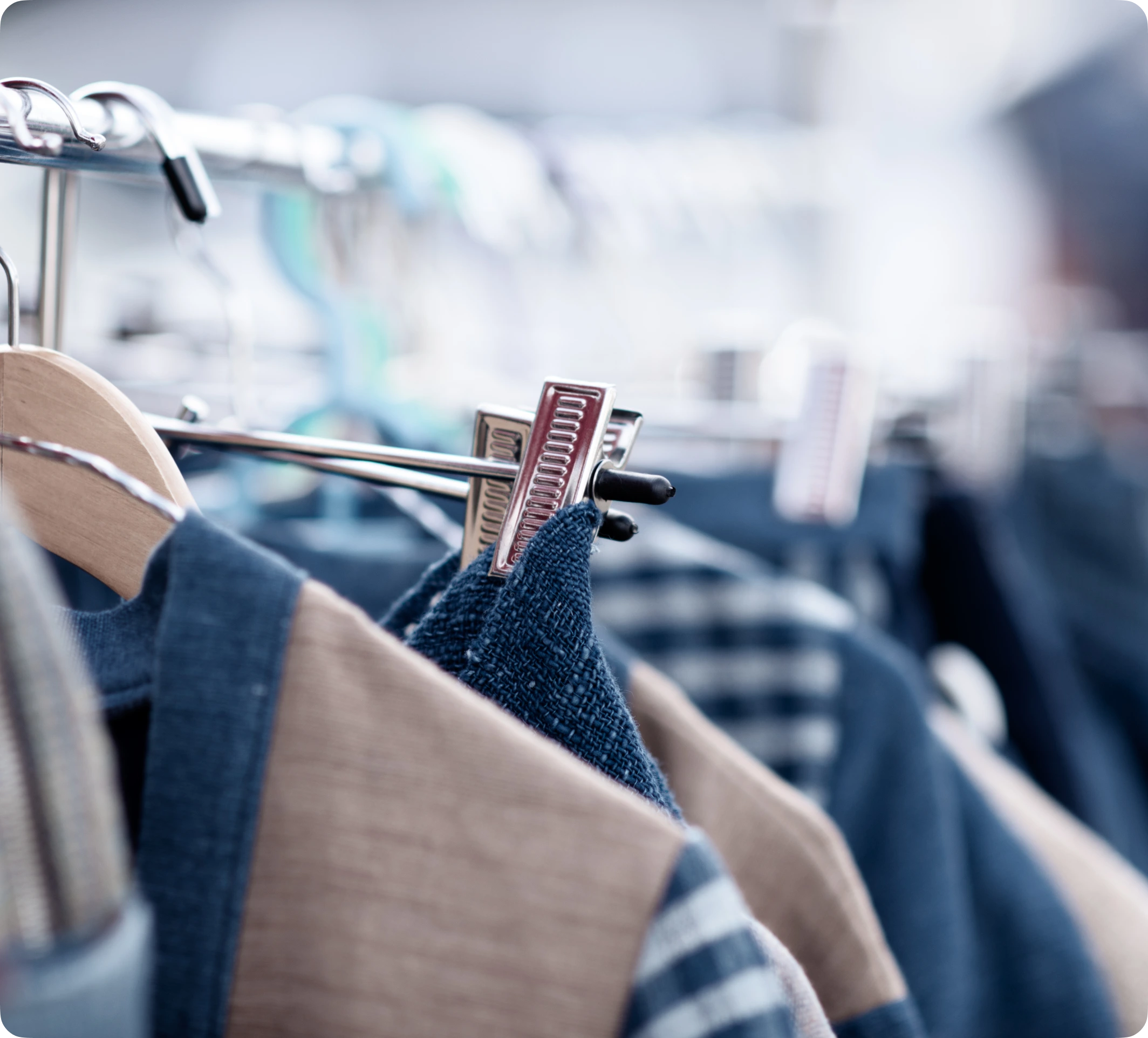 Vêtements suspendus sur cintres en bois et pinces métalliques le long d'une tringle.
