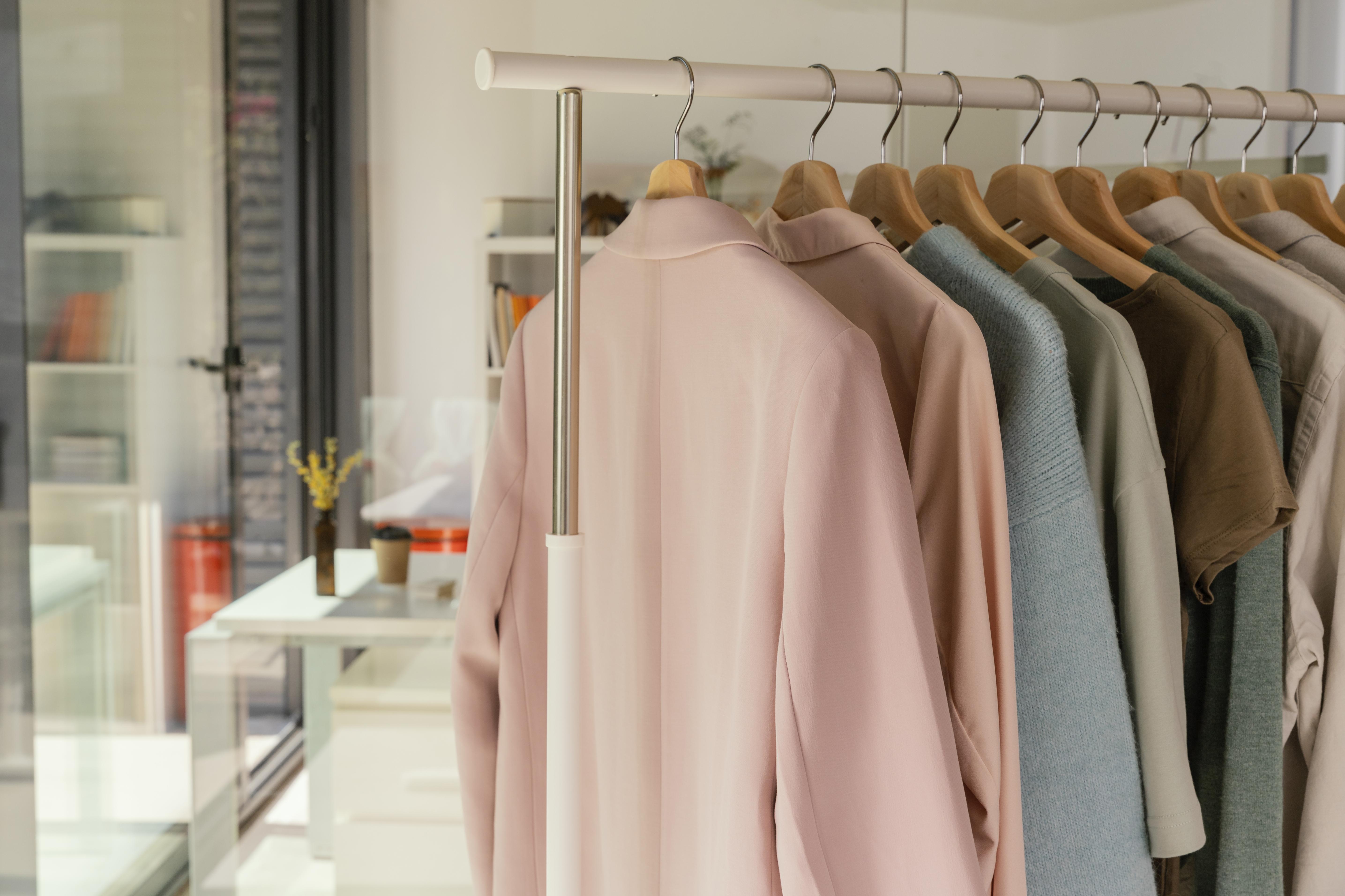 Portant de vêtements avec blazers et pulls en tons neutres, présentés sur cintres en bois dans une boutique.