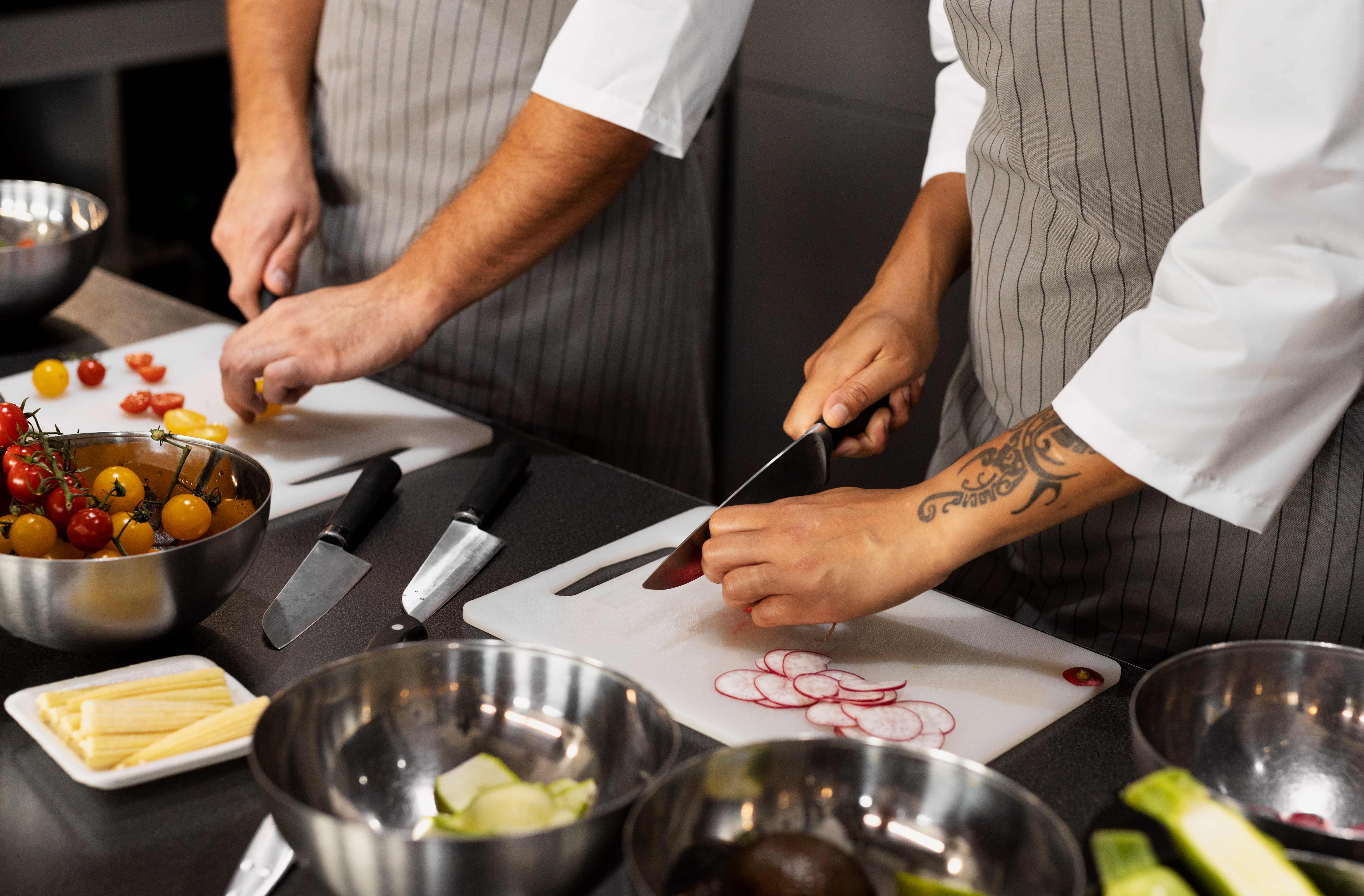 Chefs en cuisine préparant des légumes sur planche à découper, oignons rouges tranchés visibles.