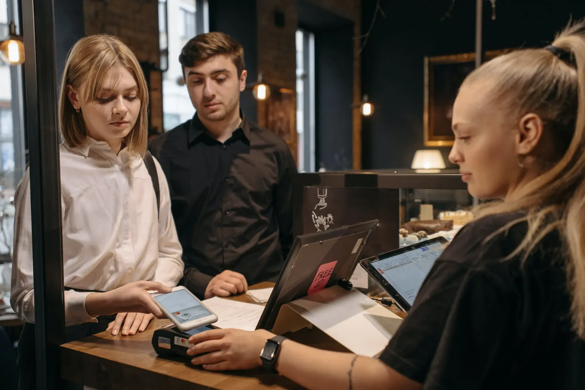Deux clients paient à la caisse avec smartphone et terminal de paiement en boutique.