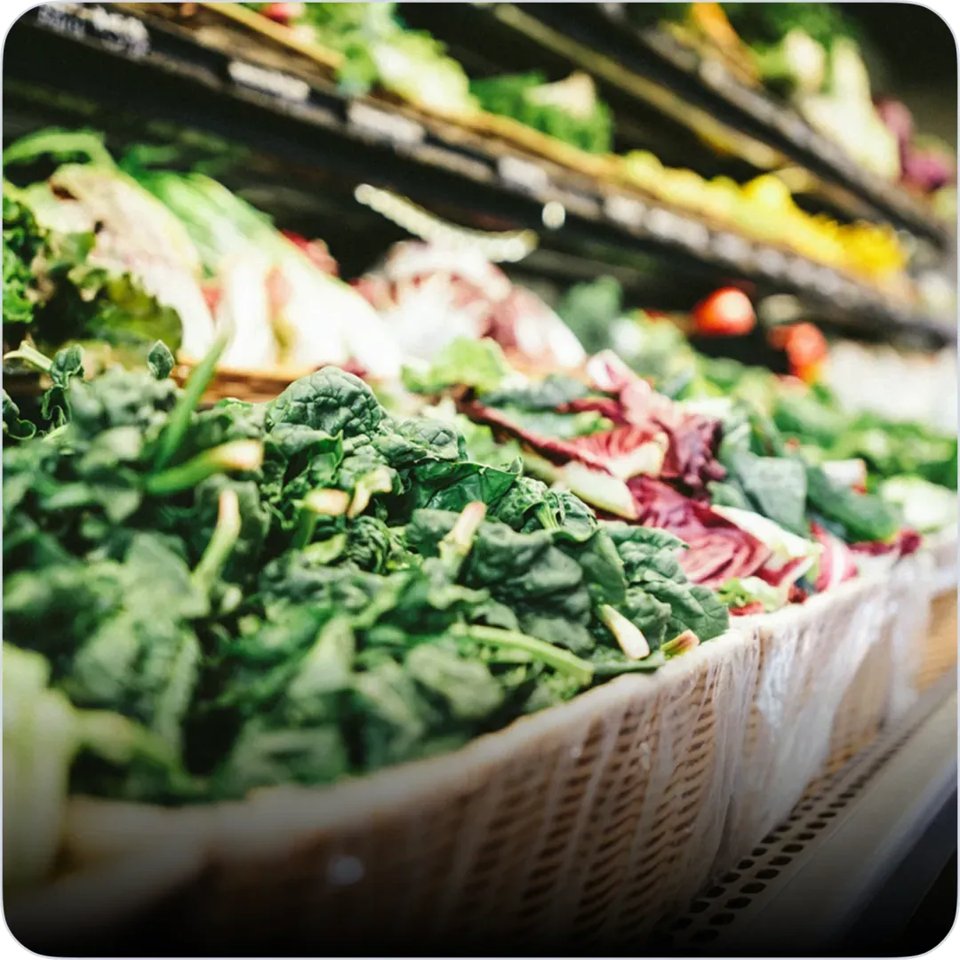 Étalage de légumes frais en vrac dans des bacs de marché : épinards, radis et autres produits.