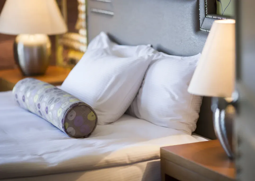 Lit d'hôtel avec oreillers blancs, coussin décoratif et lampes de chevet allumées.