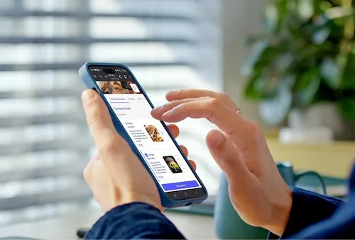Personne consultant une application de commande de repas sur smartphone en environnement de bureau.